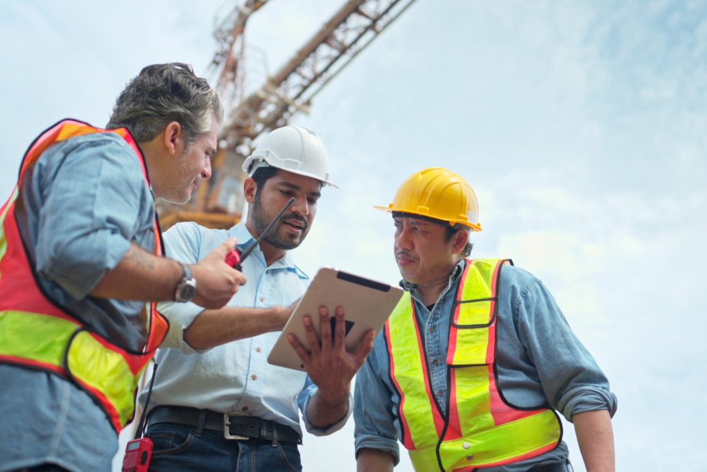 Group of workers at construction site are discussing construction progress with a tower crane in the background